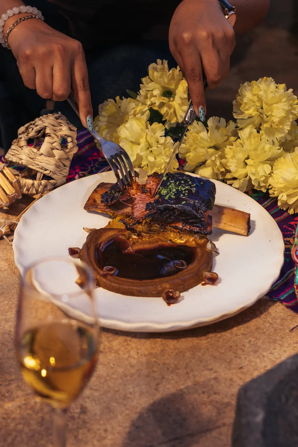Comensal cortando el short rib braseado entre flores de cempasúchil